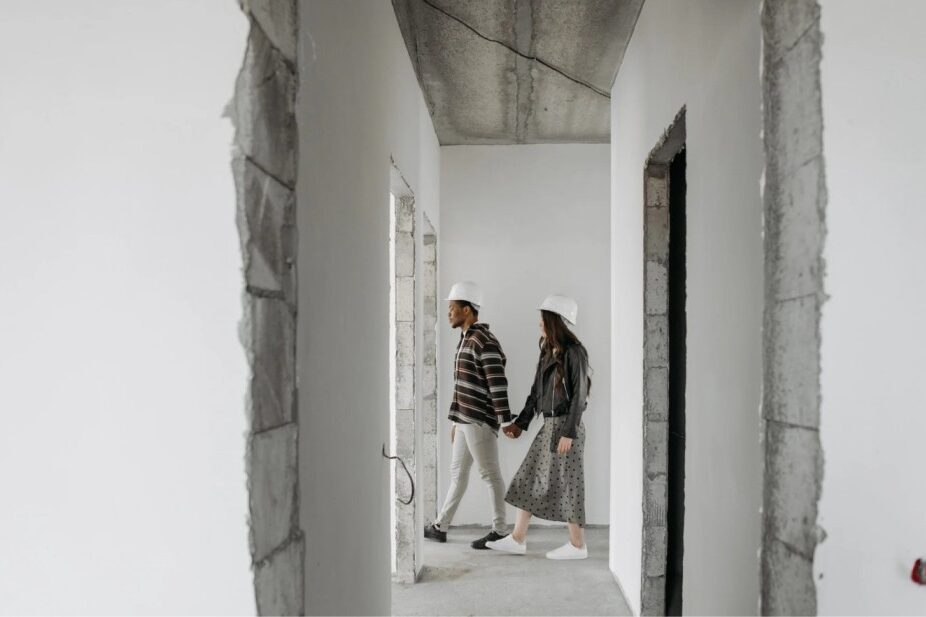 A couple walks through a nearly finished home, inspecting the walls, floors, and fixtures. The interior is almost complete, with finishing touches being made to ensure every detail is perfect before moving in.
